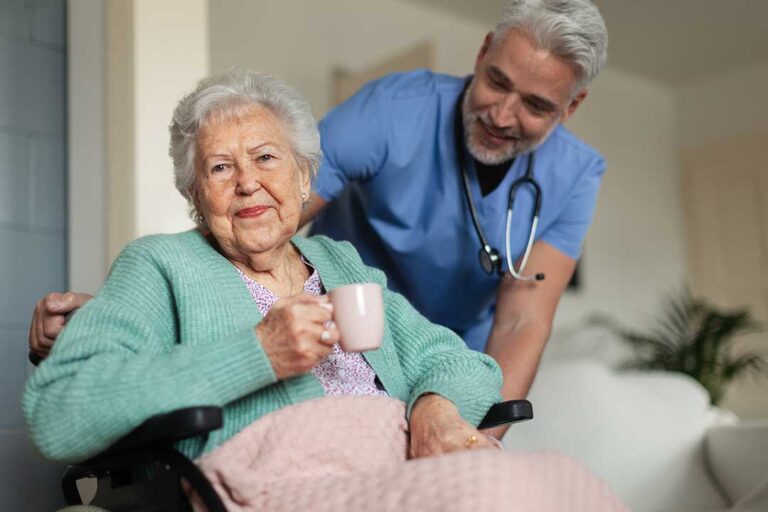 Residents and caregivers talking together in a bright common room with comfortable seating and natural light.