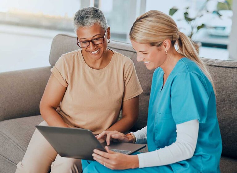 Caregiver helping an older resident walk through a bright assisted living hallway.
